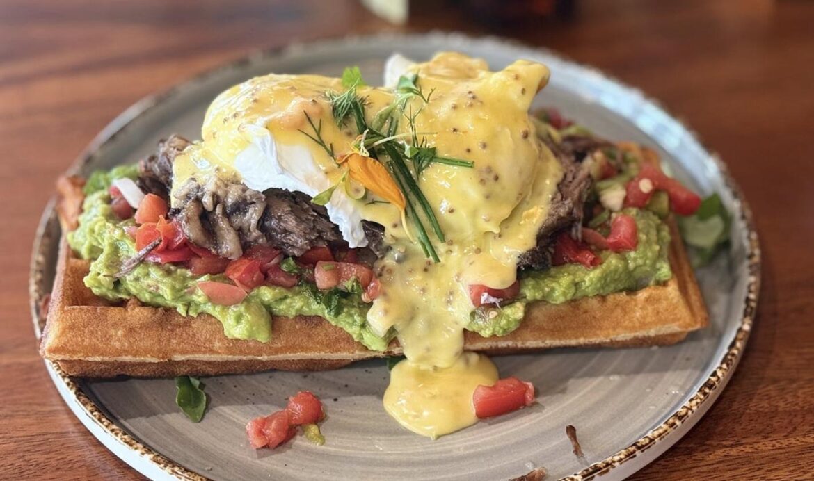 A plate of avocado toast topped with a poached egg and hollandaise sauce.