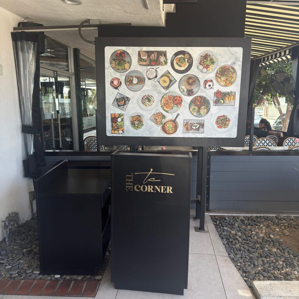 An outdoor menu board displaying food photos outside The Corner