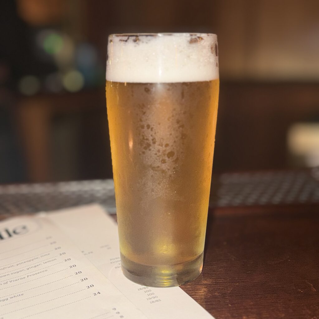 A pint of Crown & Hops' 8 Trill Pils beer on the table next to Somerville's cocktail menu.