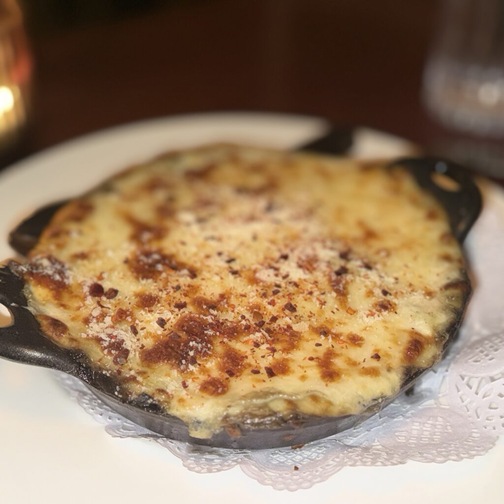 Close-up of the collard green lasagna in a mini cast-iron skillet, with a bubbling, browned cheese top dusted with parmesan and red pepper flakes.